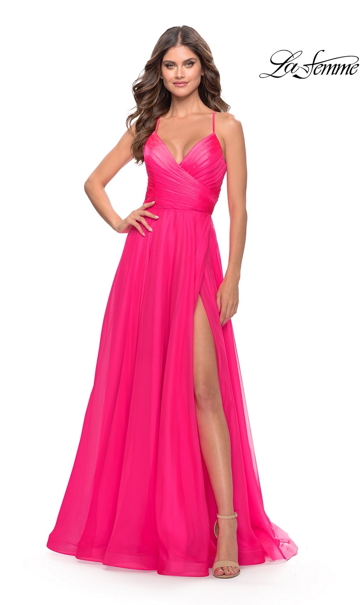A woman poses against a white background in the La Femme V-Neck Long Tulle Prom Ball Gown 30840, a bright pink, floor-length dress with spaghetti straps and a thigh-high slit.